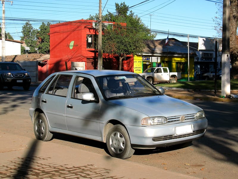 Volkswagen Gol de quatro portas prata, com linhas arredondadas, visto de frente e de lado numa rua