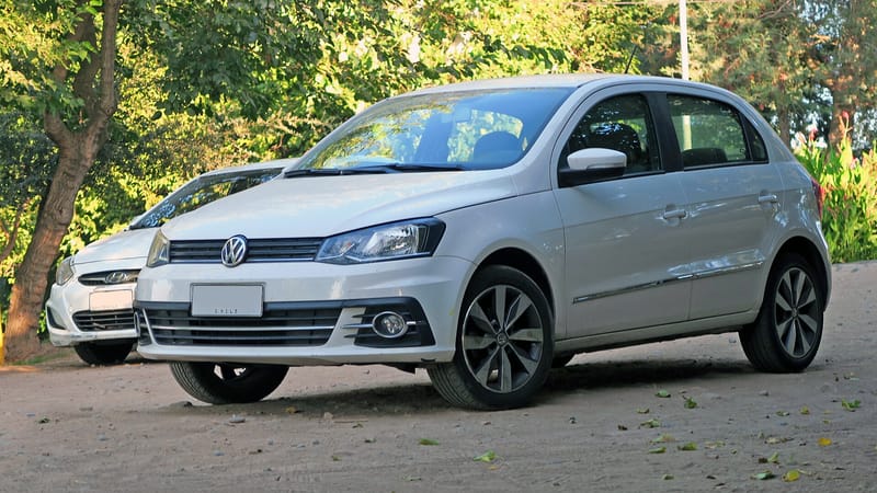 Volkswagen Gol branco de quatro portas visto de frente e de lado, com faróis alongados e grade preta fina com o emblema da marca