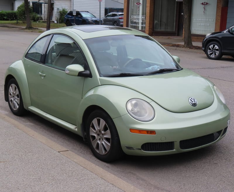 New Beetle verde-claro visto de frente e de lado, com o teto alto em arco, para-lamas salientes e faróis redondos, estacionado junto ao meio-fio