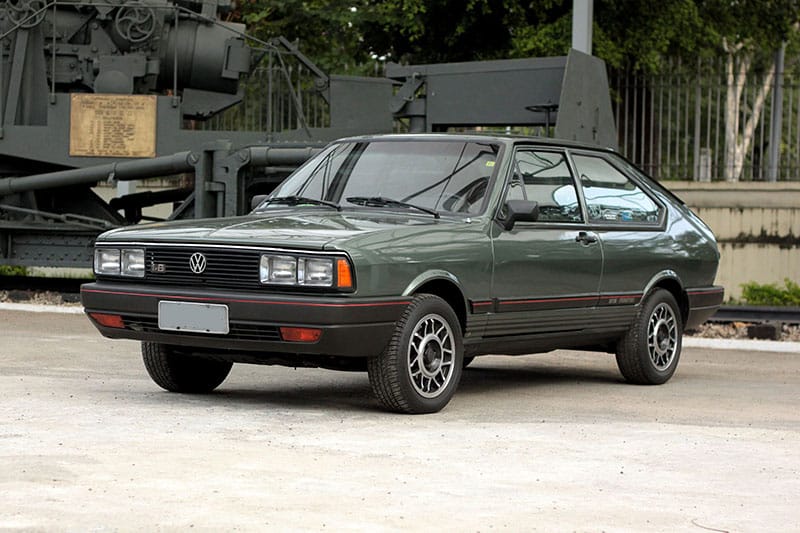 Passat GTS Pointer verde-escuro de duas portas, com emblema 1.8 na grade, faróis quadrados duplos, rodas de liga leve e friso vermelho nos para-choques, estacionado diante de uma peça de artilharia