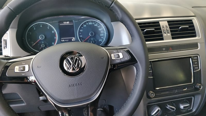 Volante de um Volkswagen Fox visto do banco do motorista, com a palavra AIRBAG gravada na parte de baixo da almofada central, botões nos raios e o painel de instrumentos ao fundo