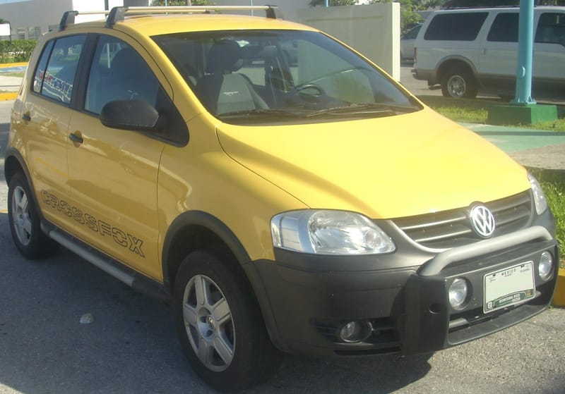Volkswagen CrossFox amarelo visto de frente e de lado, com quebra-mato preto à frente da grade, faróis auxiliares no para-choque, barras no teto e a inscrição CROSSFOX nas portas