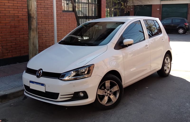 Volkswagen Fox branco de quatro portas parado junto ao meio-fio, em vista diagonal dianteira, com faróis de contorno quadrado, um friso horizontal na altura da base dos faróis e rodas de liga leve