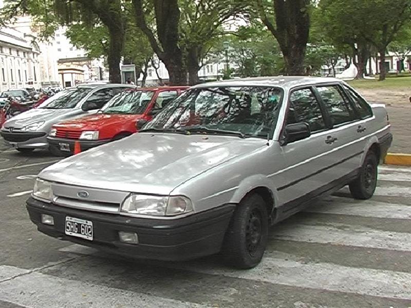 Sedã Ford prata de quatro portas estacionado sobre uma faixa de pedestres, com frente sem grade aparente, apenas uma fenda fina com o oval da Ford entre os faróis