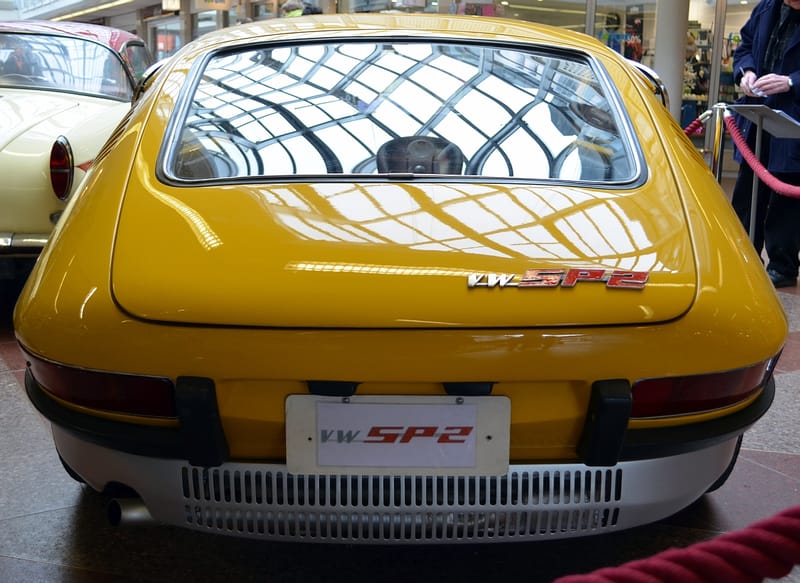 Traseira de um VW SP2 amarelo com o emblema VW SP2 na tampa, lanternas horizontais e grade de ventilação do motor sob o para-choque