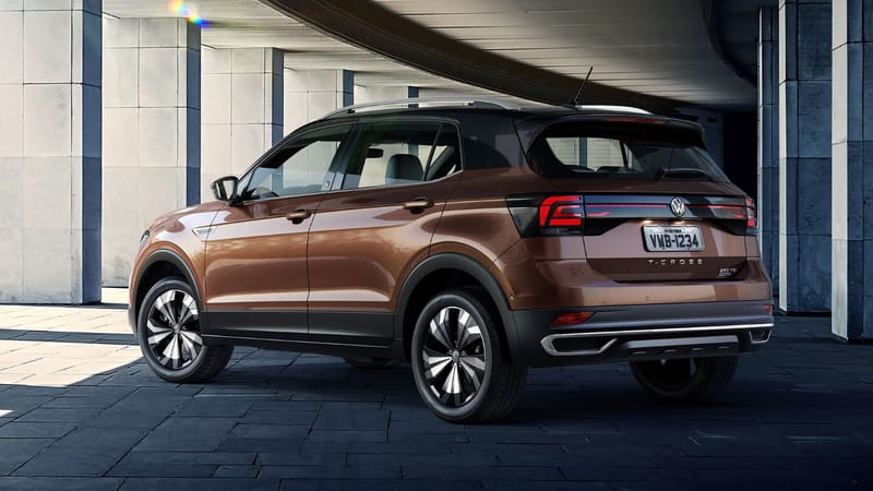 Volkswagen T-Cross marrom-bronze com teto preto, visto de trás e de lado sob uma marquise de concreto, com uma faixa vermelha refletiva horizontal num painel preto entre as lanternas e o emblema 250 TSI na tampa traseira