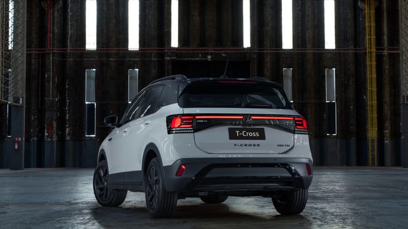 Volkswagen T-Cross branco com teto e colunas pretos, visto de trás dentro de um galpão escuro, com as lanternas ligadas por uma barra vermelha de LED acesa de ponta a ponta e o emblema 250 TSI na tampa traseira